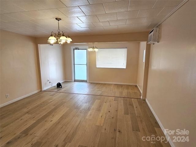 spare room with light hardwood / wood-style floors, a wall mounted air conditioner, and an inviting chandelier