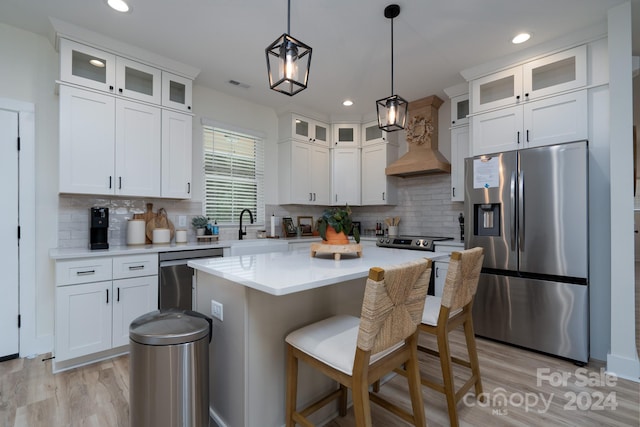 kitchen featuring appliances with stainless steel finishes, decorative backsplash, white cabinetry, a kitchen island, and premium range hood