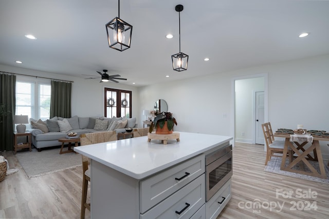 kitchen featuring pendant lighting, white cabinetry, light wood-type flooring, stainless steel microwave, and a kitchen bar