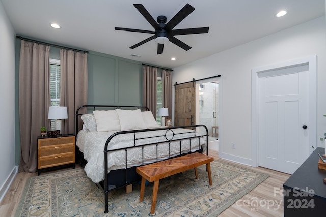 bedroom with a barn door, ceiling fan, and hardwood / wood-style flooring