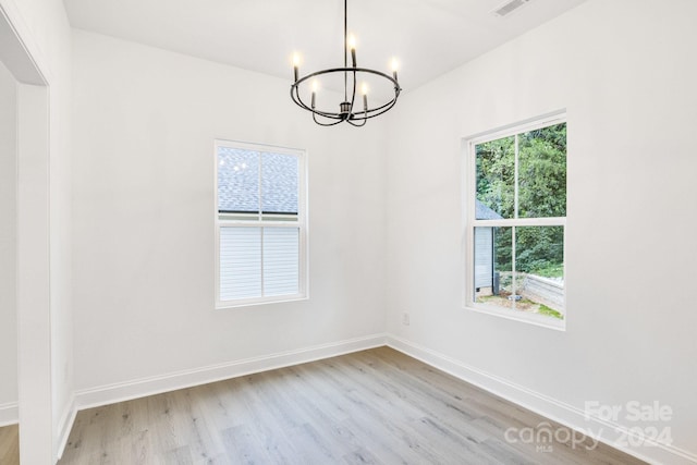 spare room with light hardwood / wood-style flooring, plenty of natural light, and a chandelier