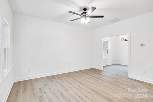 empty room with light hardwood / wood-style flooring and ceiling fan with notable chandelier