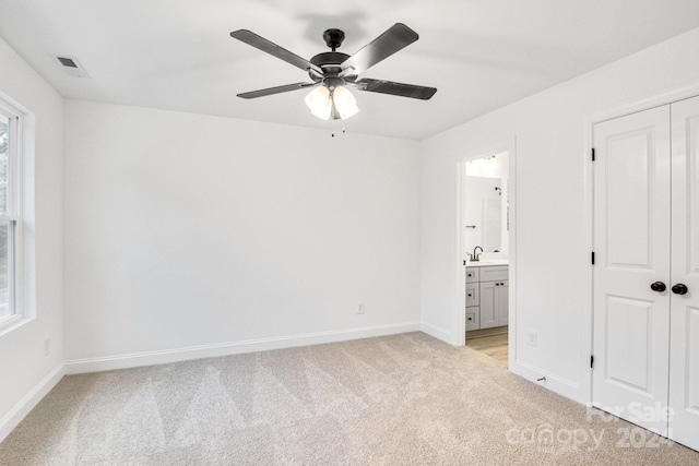 unfurnished bedroom with multiple windows, connected bathroom, light carpet, and ceiling fan