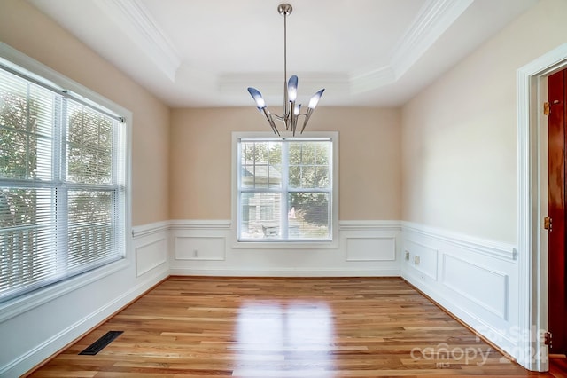 unfurnished dining area featuring crown molding, a chandelier, light hardwood / wood-style flooring, and a tray ceiling