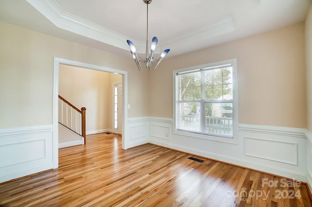 empty room with crown molding, an inviting chandelier, a raised ceiling, and light hardwood / wood-style flooring