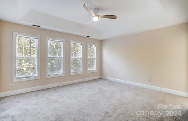 unfurnished room featuring ceiling fan, light colored carpet, a tray ceiling, and a healthy amount of sunlight