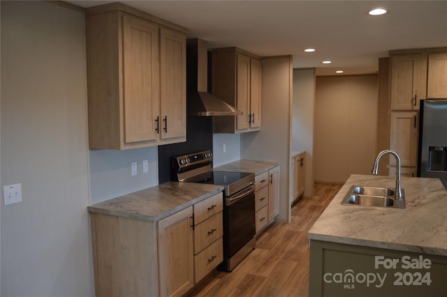 kitchen with light brown cabinets, sink, wall chimney range hood, light hardwood / wood-style flooring, and appliances with stainless steel finishes