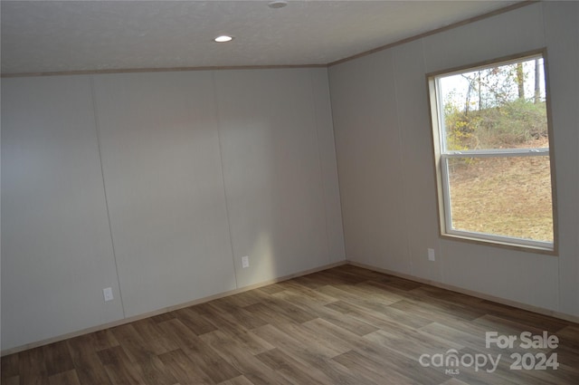 spare room featuring light hardwood / wood-style floors, ornamental molding, a textured ceiling, and vaulted ceiling