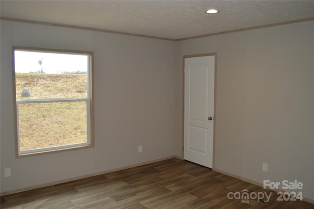 empty room with hardwood / wood-style floors, a textured ceiling, and crown molding