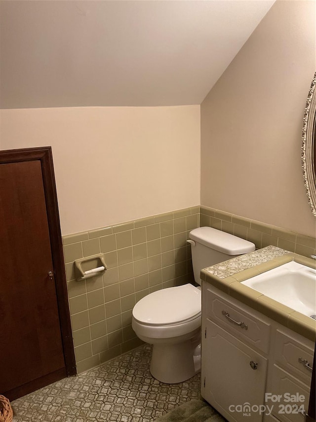 bathroom featuring vanity, vaulted ceiling, tile patterned flooring, toilet, and tile walls