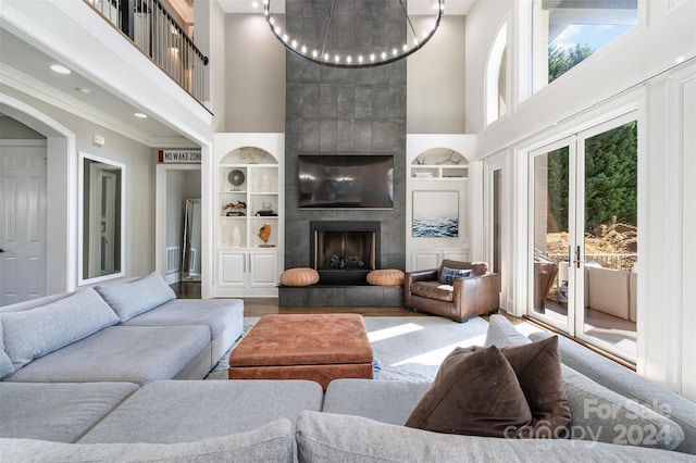 living room with ornamental molding, hardwood / wood-style floors, a towering ceiling, built in features, and a tile fireplace