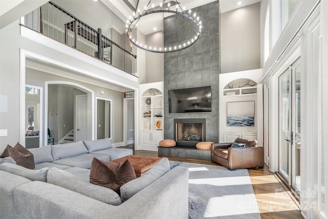 living room featuring a high ceiling, built in features, a tile fireplace, and light hardwood / wood-style flooring