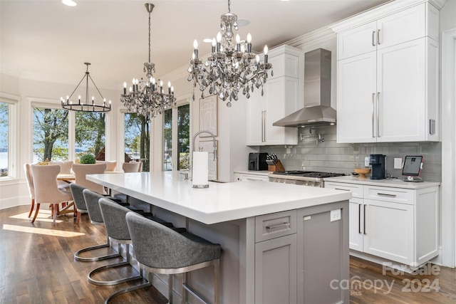 kitchen with an island with sink, wall chimney range hood, and white cabinetry