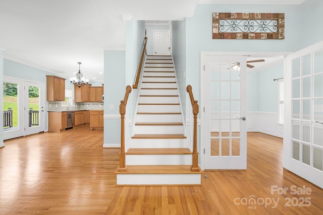 stairs featuring crown molding, wood-type flooring, ceiling fan with notable chandelier, and french doors