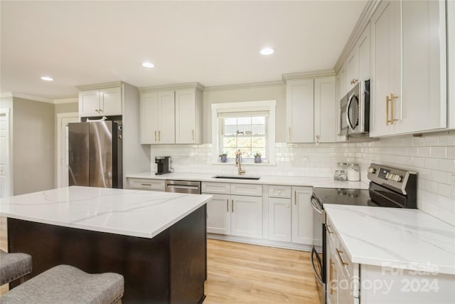 kitchen with light stone countertops, sink, appliances with stainless steel finishes, a kitchen island, and light wood-type flooring