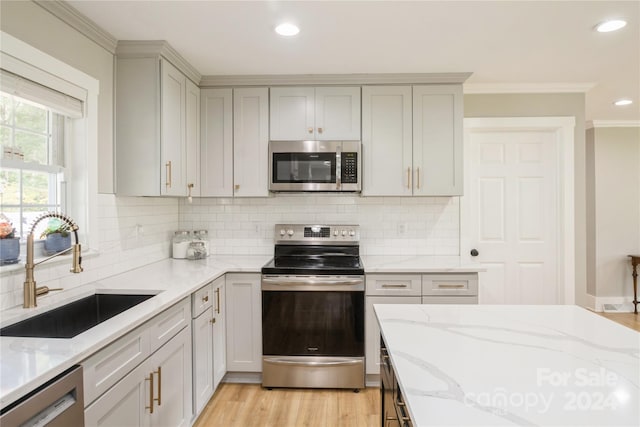 kitchen featuring light wood-type flooring, light stone counters, stainless steel appliances, crown molding, and sink