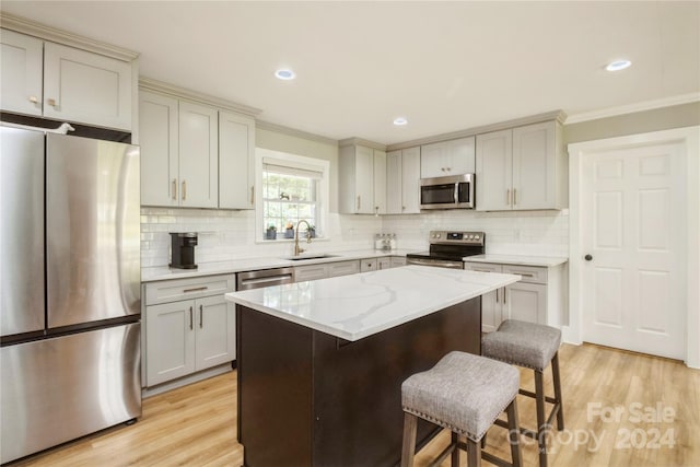 kitchen featuring light stone counters, stainless steel appliances, sink, a center island, and light hardwood / wood-style floors