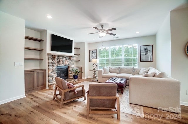 living room with light wood-type flooring, a stone fireplace, ceiling fan, and built in features