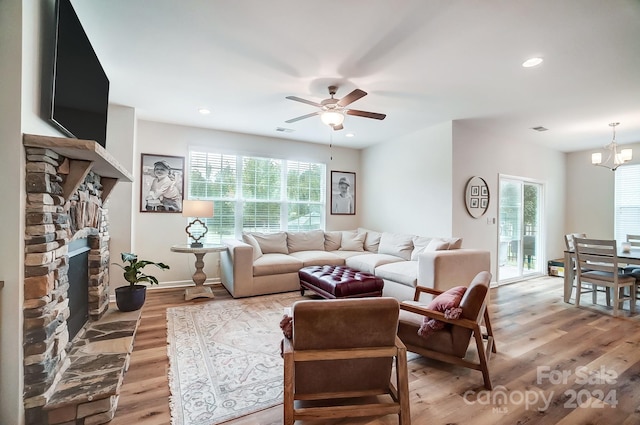 living room featuring a stone fireplace, ceiling fan with notable chandelier, light hardwood / wood-style floors, and plenty of natural light