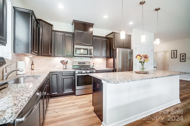 kitchen featuring appliances with stainless steel finishes, a center island, light hardwood / wood-style flooring, decorative light fixtures, and sink