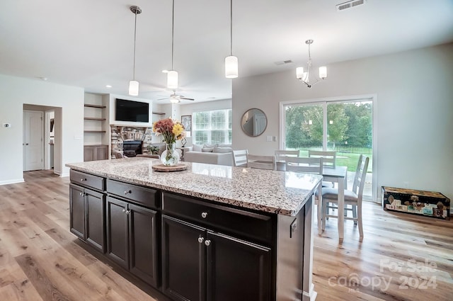 kitchen with light stone counters, a stone fireplace, a kitchen island, pendant lighting, and light hardwood / wood-style flooring