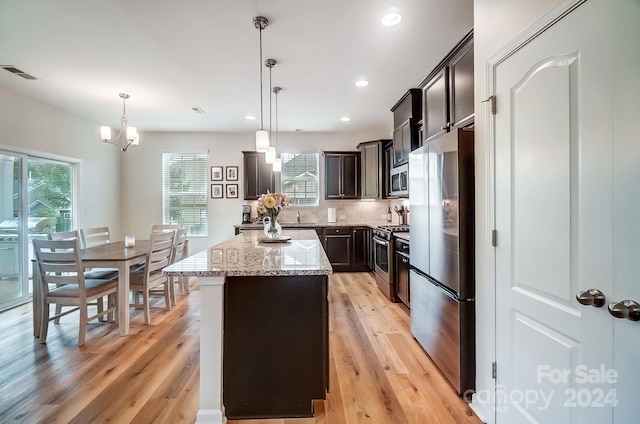 kitchen featuring appliances with stainless steel finishes, a center island, pendant lighting, and light hardwood / wood-style flooring