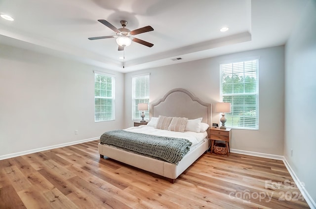 bedroom featuring ceiling fan, a raised ceiling, light hardwood / wood-style floors, and multiple windows