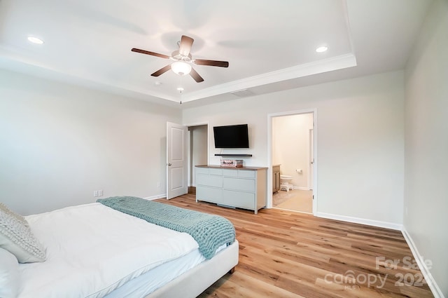 bedroom with light wood-type flooring, connected bathroom, a tray ceiling, and ceiling fan