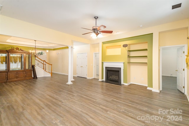 unfurnished living room with ceiling fan with notable chandelier, hardwood / wood-style flooring, built in shelves, a tray ceiling, and decorative columns