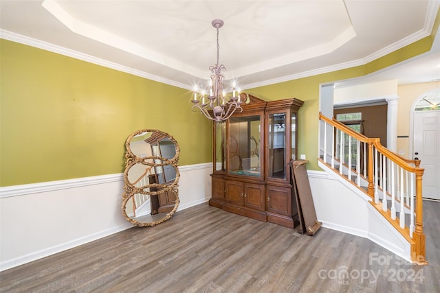 dining area with ornate columns, an inviting chandelier, wood-type flooring, a tray ceiling, and ornamental molding