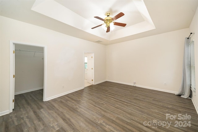 interior space with a walk in closet, a tray ceiling, ceiling fan, dark wood-type flooring, and a closet