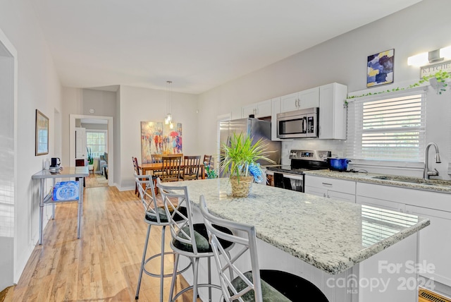 kitchen featuring light hardwood / wood-style floors, sink, stainless steel appliances, hanging light fixtures, and white cabinetry