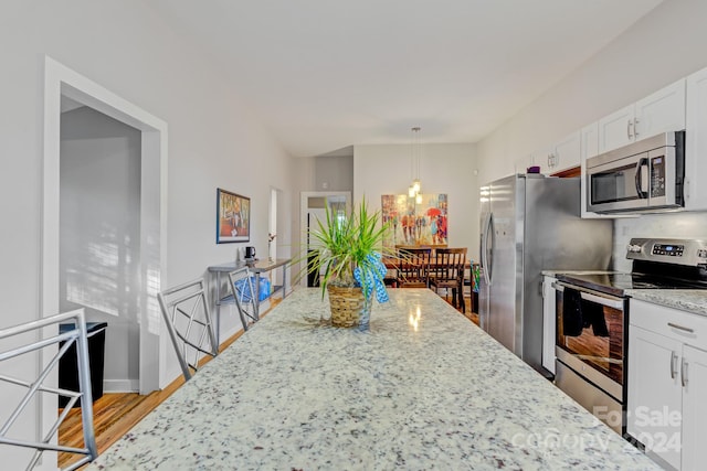 kitchen with light wood-type flooring, decorative light fixtures, stainless steel appliances, light stone countertops, and white cabinetry