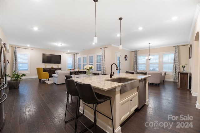 kitchen with dark hardwood / wood-style floors, a kitchen island with sink, sink, decorative light fixtures, and light stone countertops