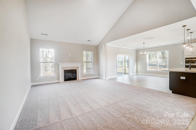 unfurnished living room with plenty of natural light, light colored carpet, ornamental molding, and a chandelier