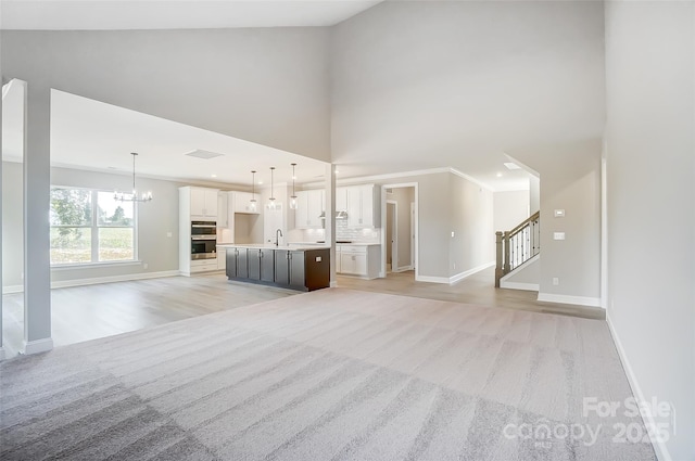 unfurnished living room with light colored carpet, a towering ceiling, sink, and an inviting chandelier