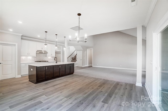 kitchen with ornamental molding, sink, pendant lighting, a center island with sink, and white cabinetry