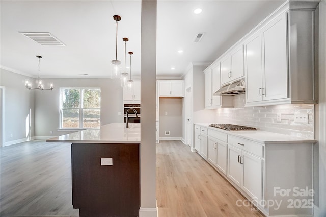 kitchen featuring crown molding, hanging light fixtures, light hardwood / wood-style flooring, tasteful backsplash, and white cabinetry