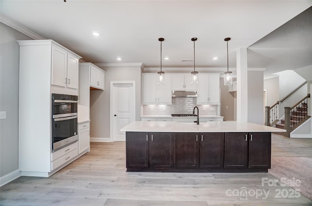 kitchen with double oven, a center island with sink, white cabinets, and decorative light fixtures