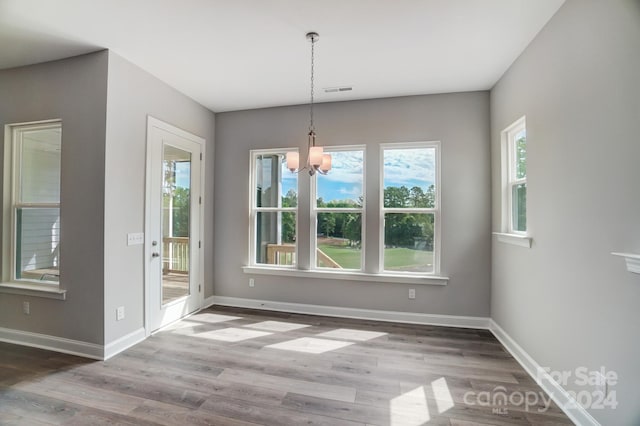 unfurnished dining area featuring a wealth of natural light, hardwood / wood-style floors, and a notable chandelier