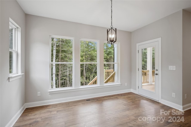 unfurnished dining area with hardwood / wood-style flooring, an inviting chandelier, and plenty of natural light