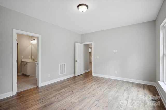 unfurnished bedroom with multiple windows, sink, connected bathroom, and light wood-type flooring