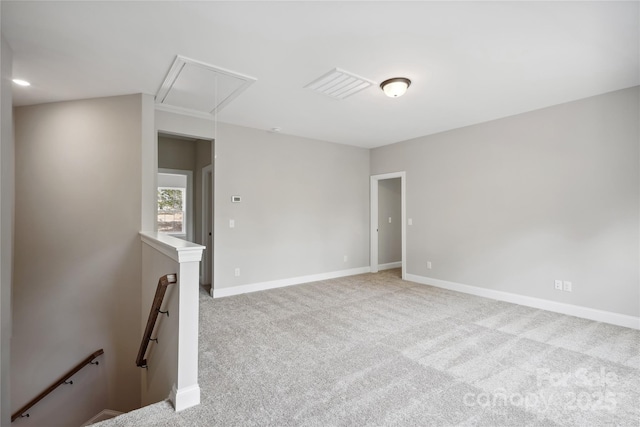 carpeted empty room with attic access, visible vents, and baseboards