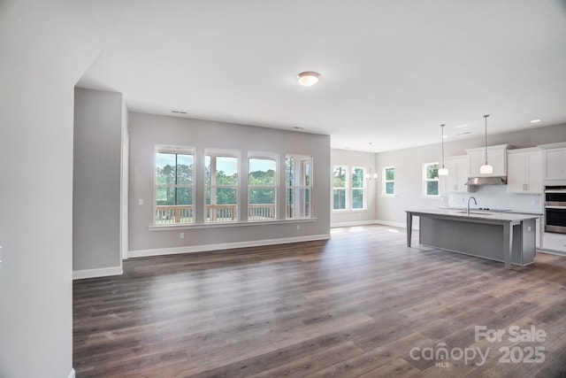 kitchen with a center island with sink, dark wood finished floors, hanging light fixtures, white cabinets, and baseboards