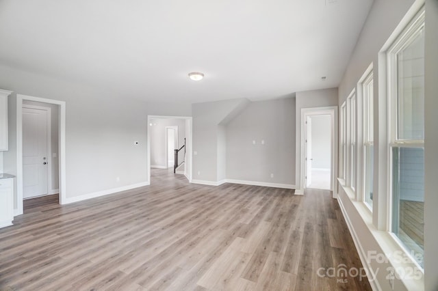 unfurnished room featuring stairs, light wood finished floors, and baseboards