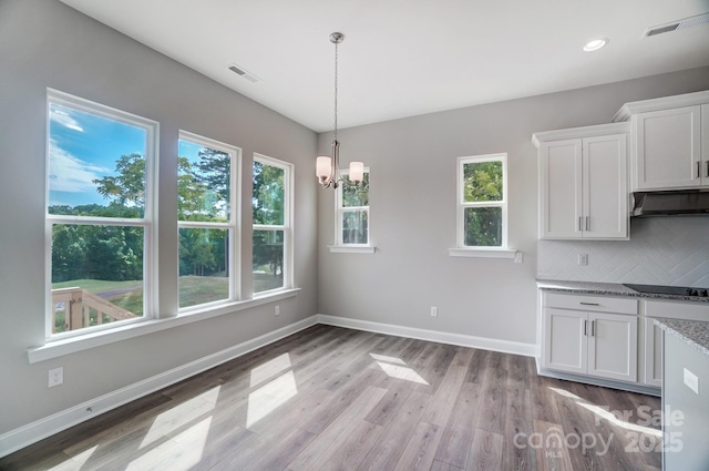 unfurnished dining area featuring light wood-style floors, plenty of natural light, an inviting chandelier, and baseboards