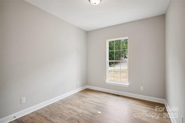 empty room with wood finished floors, visible vents, and baseboards