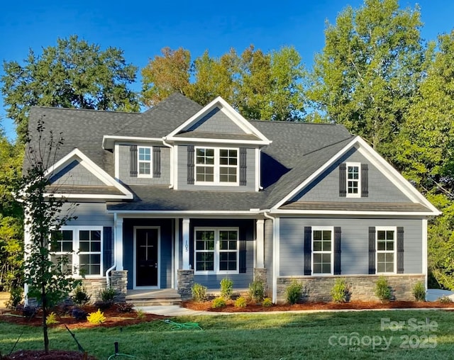 craftsman-style house with stone siding, a shingled roof, and a front yard