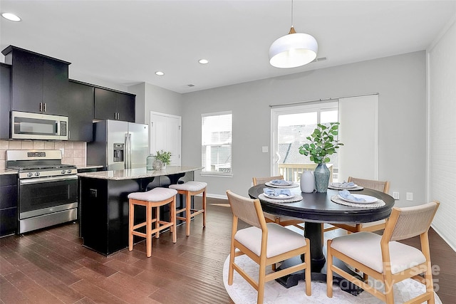 kitchen with appliances with stainless steel finishes, a center island, decorative light fixtures, backsplash, and dark hardwood / wood-style floors