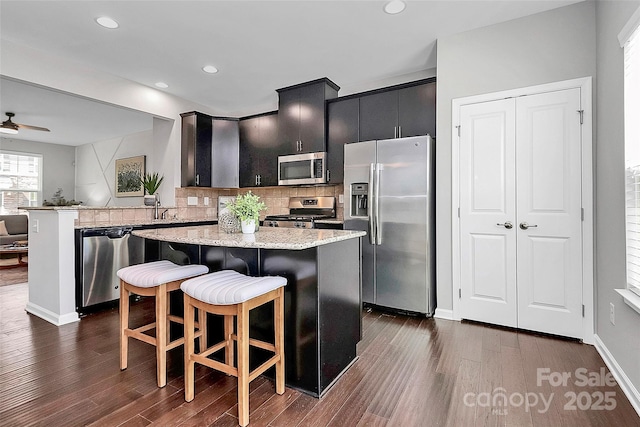 kitchen with dark wood-type flooring, decorative backsplash, appliances with stainless steel finishes, and a center island